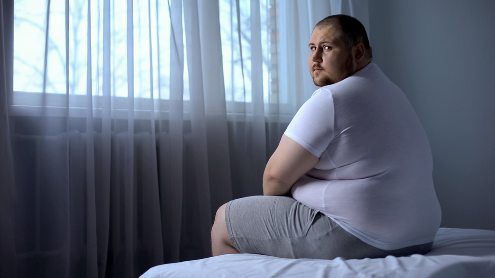 overweight man sitting in bed thinking